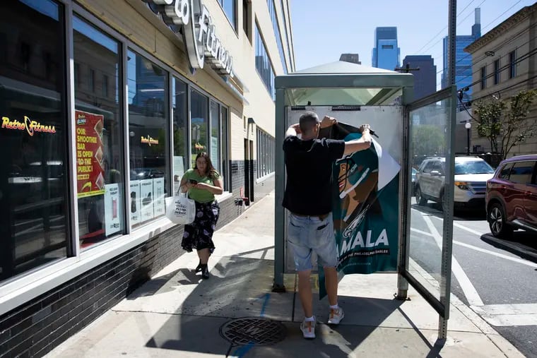 Stephen Casey takes down a counterfeit Philadelphia Eagles and Kamala Harris ad from a bus shelter at 16th and Spring Garden Streets in Philadelphia on Monday, Sept. 2, 2024. Casey said, “The way I look at it, I was just returning things to the status quo.”