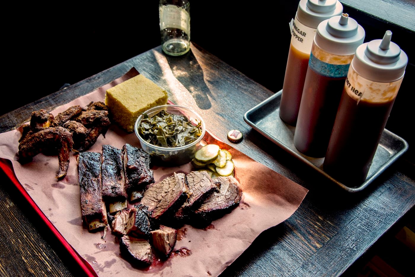 A plater of brisket, ribs an Korean wings, with dill pickles, cornbread, and collared greens fixins at Mike's BBQ.