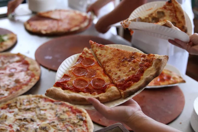 Waitresses at Sam's Pizza Palace fill their hands with plates of pizza slices from the table filled with pizza pies.