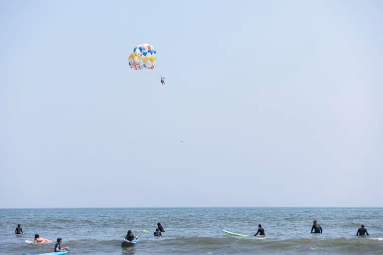 People parasail as surfers watch in Ocean City, N.J.