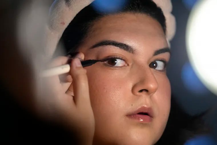 Daniella López White, of Hawaii, uses a mirror while applying makeup at her apartment in Boston. López White, who graduated from Emerson College in Boston and is on a tight budget, said TikTok influencers have helped her with tips on how to find affordable clothes at places like H&M and thrift shops. She buys makeup brands at CVS based on influencer advice.