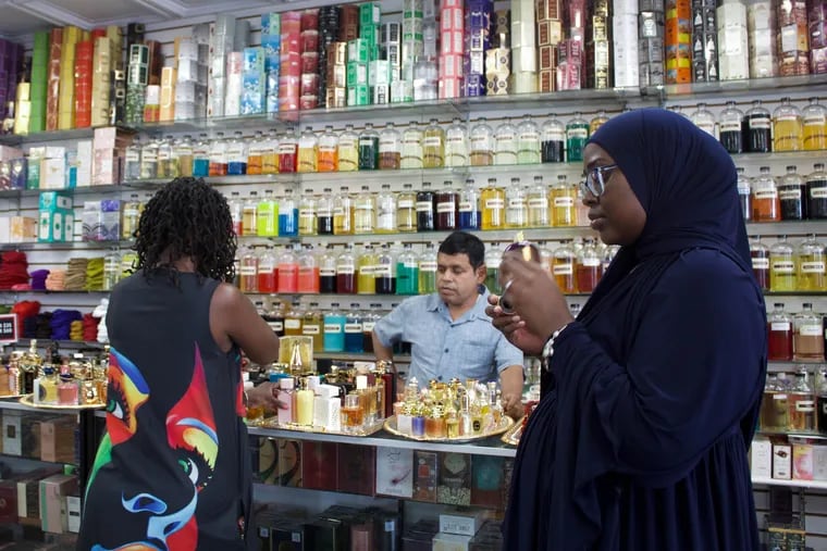 Mohammad Khan (center), owner of Al-Amanah in West Philadelphia, helps customers select perfume oils in his store.