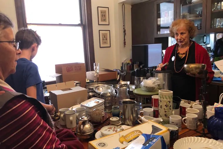 Karen Mulhauser (right) makes one of her announcements by pinging her Tibetan singing bowl. She's giving away her belongings to prepare to move to condo after 45 years in her D.C. home.