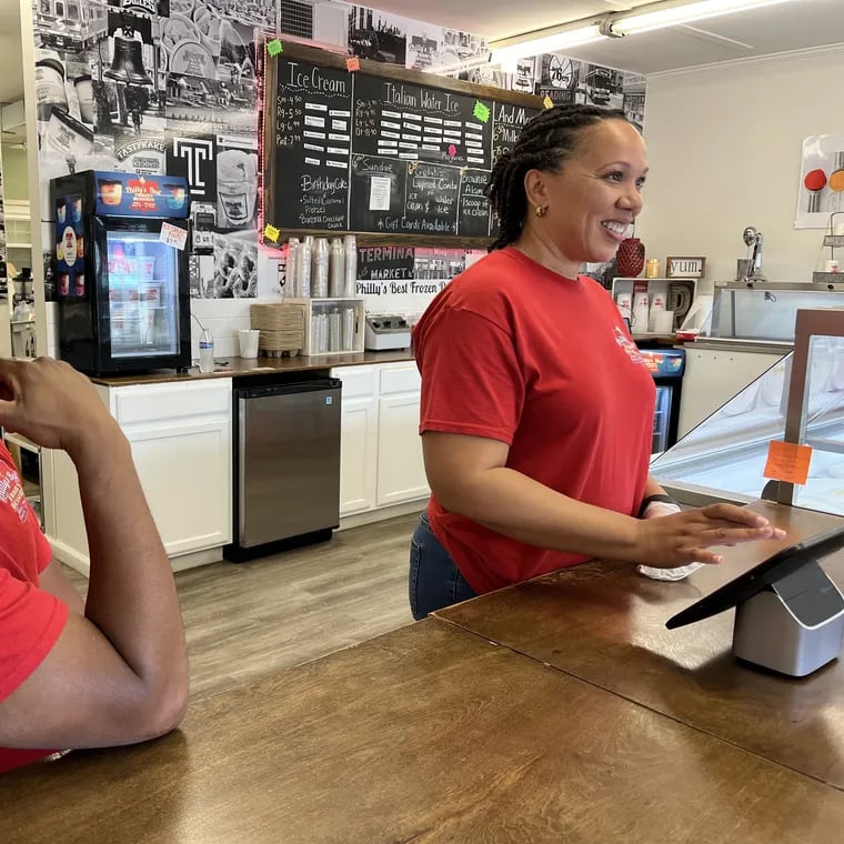 Philadelphia area expats Rodney and Tonya Daisey working behind the counter of Philly's Best Frozen Desserts, the water ice and ice cream shop they own and operate in Louisville, Kentucky. Behind them is a mural of well-known Philadelphia images.