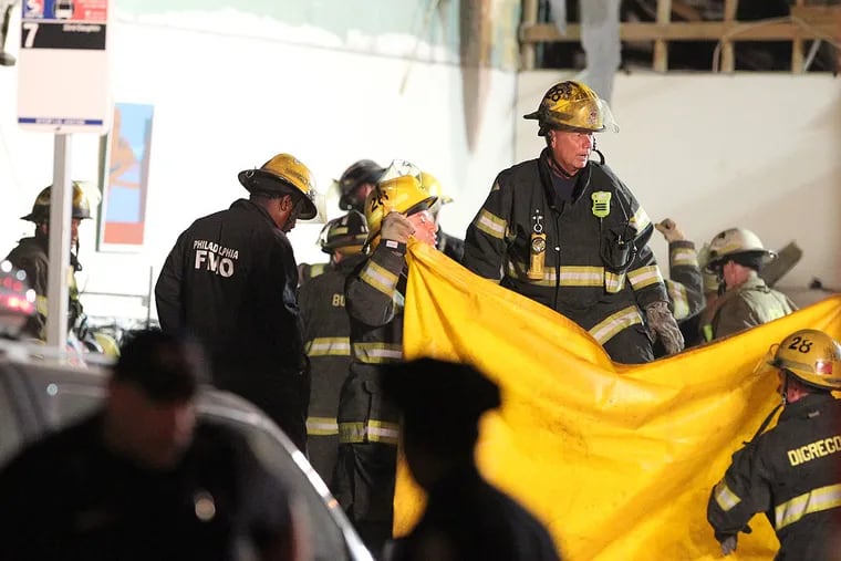 The death toll in up to six.  Fire fighters hold up a yellow tarp as they prepare to remove another body from the collapsed building at 22nd and Market Sts.   ( CHARLES FOX / Staff Photographer )