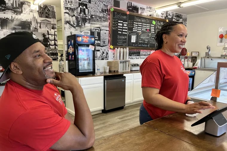Philadelphia area expats Rodney and Tonya Daisey working behind the counter of Philly's Best Frozen Desserts, the water ice and ice cream shop they own and operate in Louisville, Kentucky. Behind them is a mural of well-known Philadelphia images.