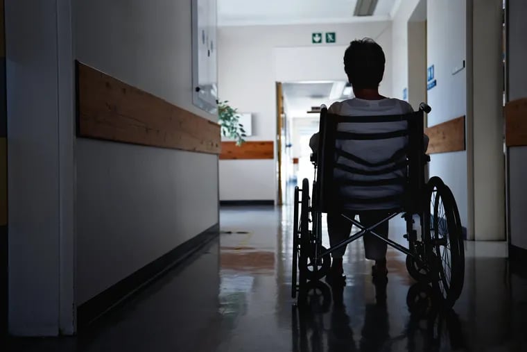 A patient in a wheelchair sits in the hallway of a hospital or nursing home.