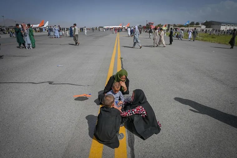 Afghan people sit along the tarmac as they wait to leave the Kabul airport on Aug. 16.