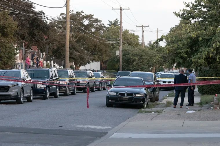 Neighbors (left) watch as police investigate the scene in front of 4011 Meridian St. in Philadelphia where a 7-month-old baby was shot on Thursday evening.