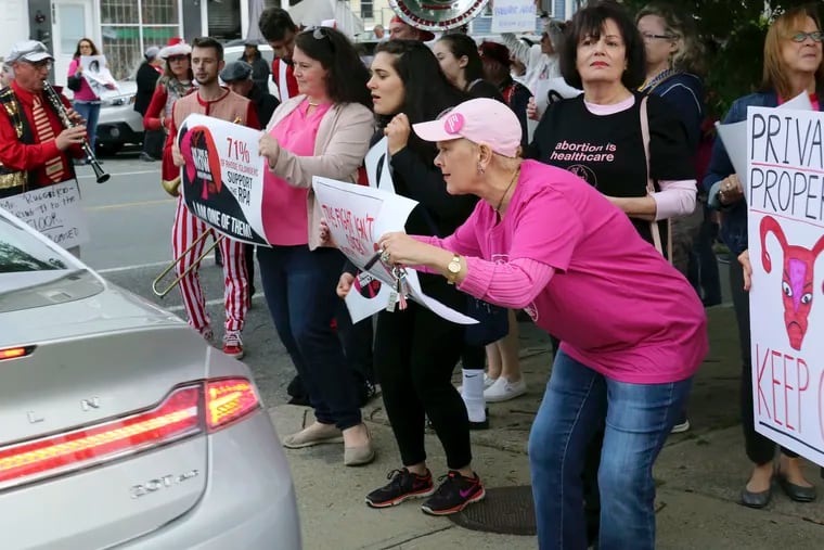 In this Thursday, May 23, 2019, photo, Nancy St Germain, 71, right, of Warwick, R.I., leans forward to show her sign to a driver leaving a fundraiser for the Rhode Island Senate Democrats political action committee in Providence, R.I. Her sign reads, "This fight isn't over." Protesters gathered at the fundraiser to pressure legislative leaders to bring a bill seeking to protect abortion rights to the Senate floor for a vote. (AP Photo/Jennifer McDermott)
