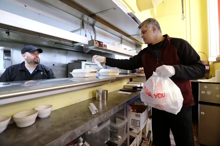 In this Tuesday, March 31, 2020, photo, Glen Quadros, right, owner of the Great American Diner & Bar, checks a takeout order as cook Arturo Aguilar looks on in Seattle. New Jersey Gov. Phil Murphy signed a bill Wednesday that prohibits the sale of single-use plastic carryout bags, paper bags, and polystyrene foam containers. (AP Photo/Elaine Thompson)