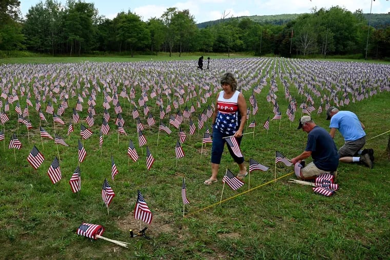 Gold Star Mother Kathy Hause Walker works with her husband, Patrick Walker (right) and Randy Musser (center)  president of the Patriot Park foundation, to plant more than 7,000 small US flags near the Flight 93 National Memorial in Somerset County Aug. 23, 2021, as a tribute to all the military members who have died during the global War on Terror following the Sept.11, 2001 attacks.