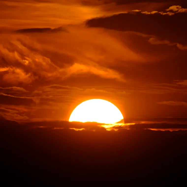 The setting sun illuminates the clouds over the Rocky Mountains after a third straight day of record-breaking heat Sunday in Denver.