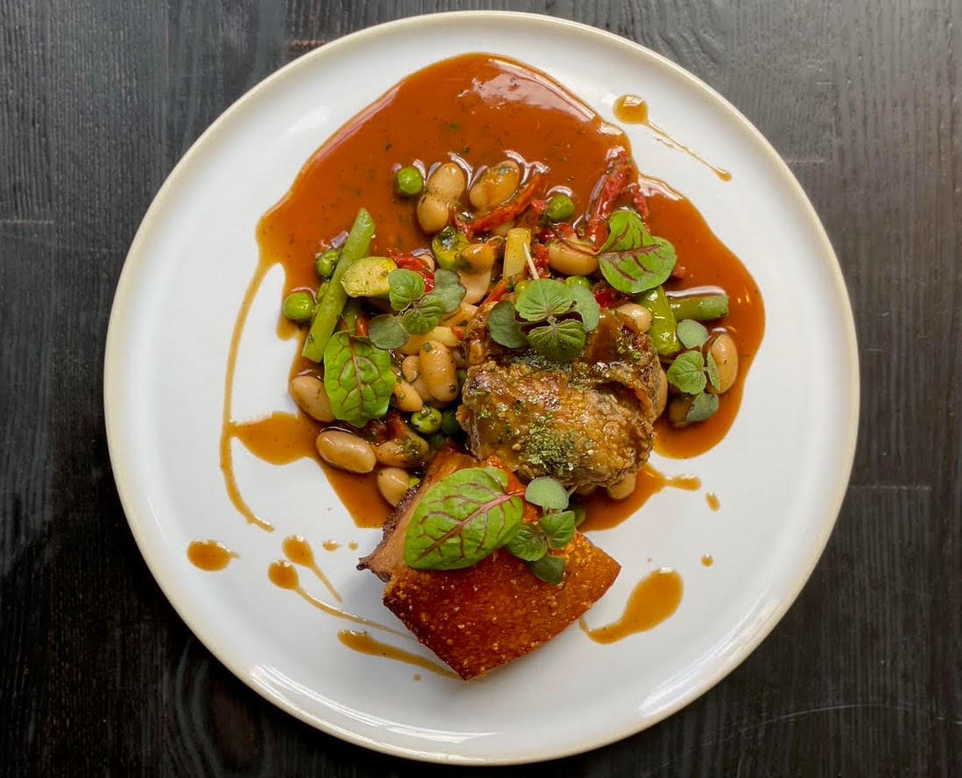 The crispy pork entree at Forsythia consists of braised-then-fried pork cheeks served with pork belly, a spring pea ragout, black pepper jus, and hot honey.