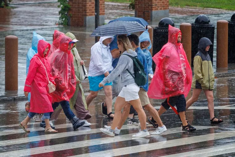 Visitors wear ponchos to protect themselves from the rain as they cross Sixth and Market Streets on Thursday, which so far has been a wetter day than Friday in Philly.