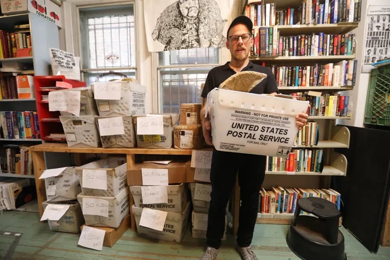 Keir Neuringer and the bins of unmailed packages of books that were supposed to go out to PA prison inmates but were held back because of a lockdown, at his Philadelphia office Thursday September 13, 2018. DAVID SWANSON / Staff Photographer .