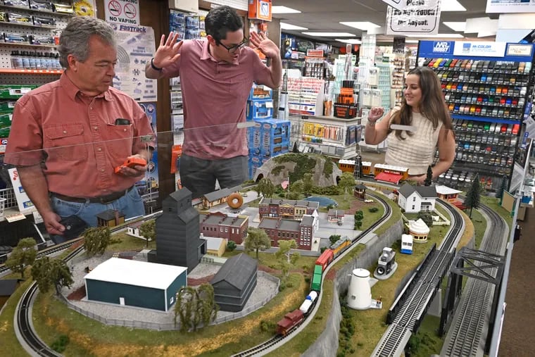 Marketing manager Jack Lynch (left) operates the remote control as owners Alan and Emily Bass (right) watch the action on the in-store train layout with O, N, and HO scale railroads at AAA Hobbies and Crafts in Magnolia, N.J. on June 11, 2024. The three-generation, family-owned shop is marking its 40th anniversary on June 22 and 23 with a massive hobby party to thank the local community for their support over the last four decades. They stock extensive model railroading supplies and brands including Bachmann, Atlas, Lionel, Preiser, Woodland Scenics, Peco, and dozens more, and accessories including scenery/landscaping and detail parts for all railroad layouts.