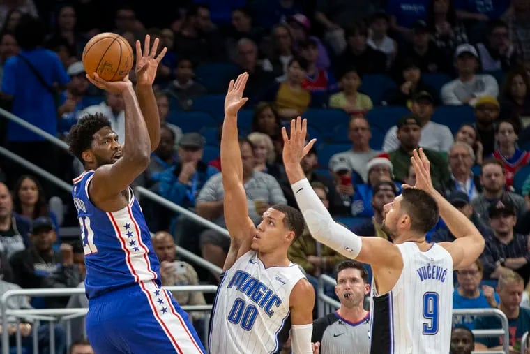 Center Joel Embiid (21) shoots over Orlando's Aaron Gordon (00) and Nikola Vucevic (9) during the first half of the Sixers' 98-97 loss Friday night.