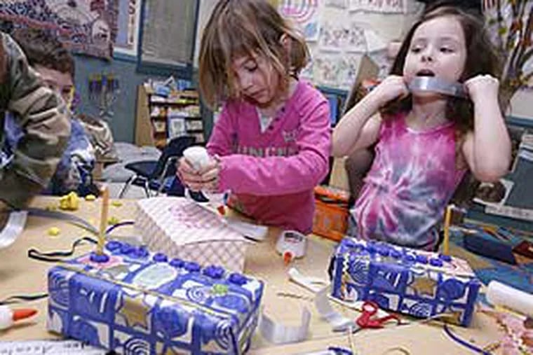 Hannah Weber (left) and  Lark Staloff-O'Brien  put finishing touches on the menorahs that their kindergarten class made from recyclable materials.  The Cherry Hill students, and Jews the world over, will begin the celebration of Hanukkah on Tuesday at sundown, with candles to be lit for eight nights.