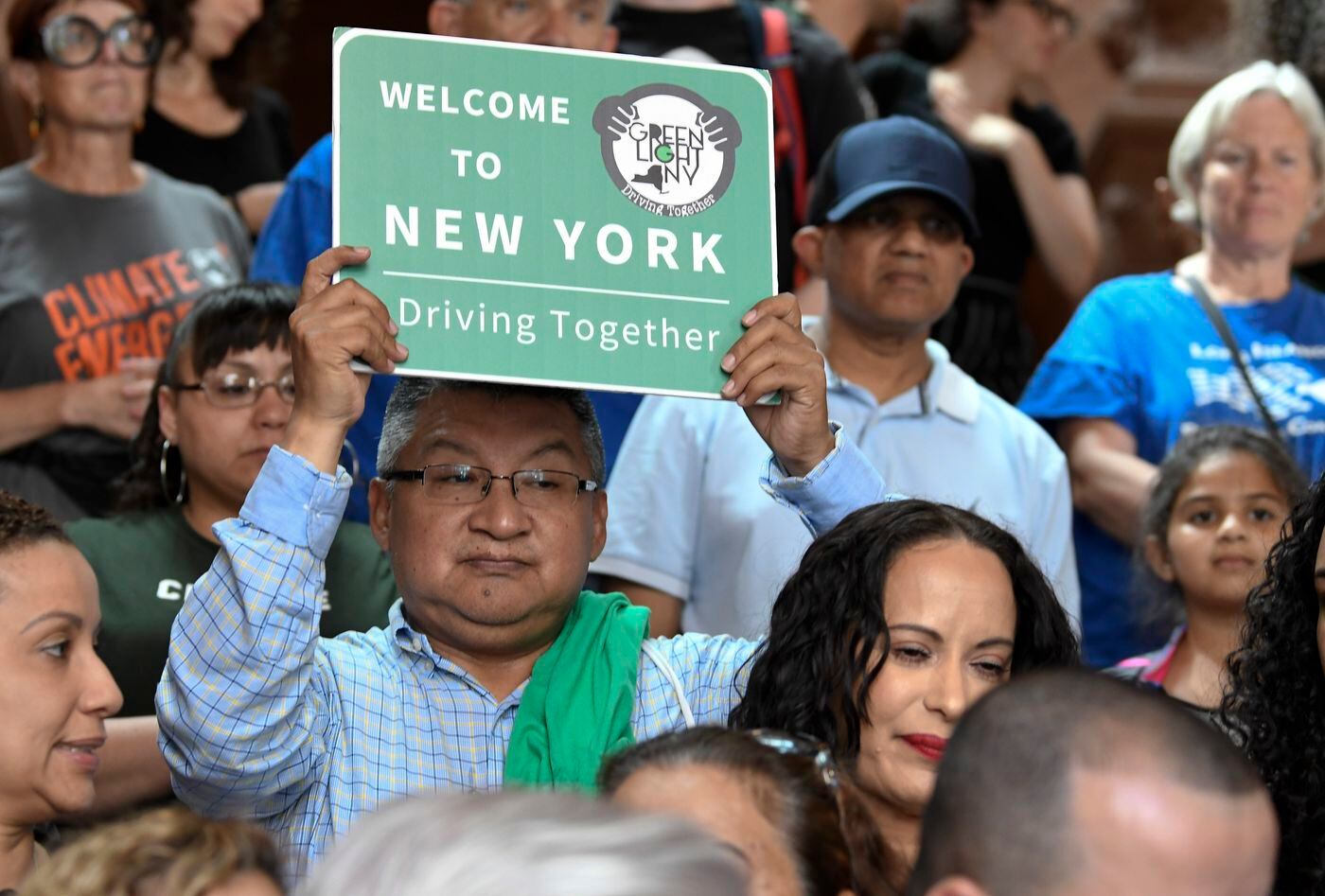 In New York, a protester holds a sign in 2019 as members of the state Assembly speak in favor of legislation of the Green Light Bill, granting undocumented immigrant driver's licenses during a rally at the state Capitol, in Albany. The bill passed , allowing applicants without a Social Security number to apply for a driver's license.