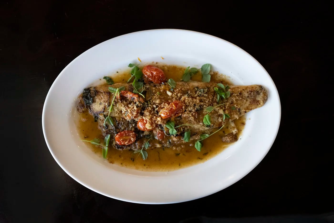 A meaty branzino fillet was topped with a brothy butter sauce of citrus and tomatoes and crunchy oreganata crumbs at Queen Bean Bistro.