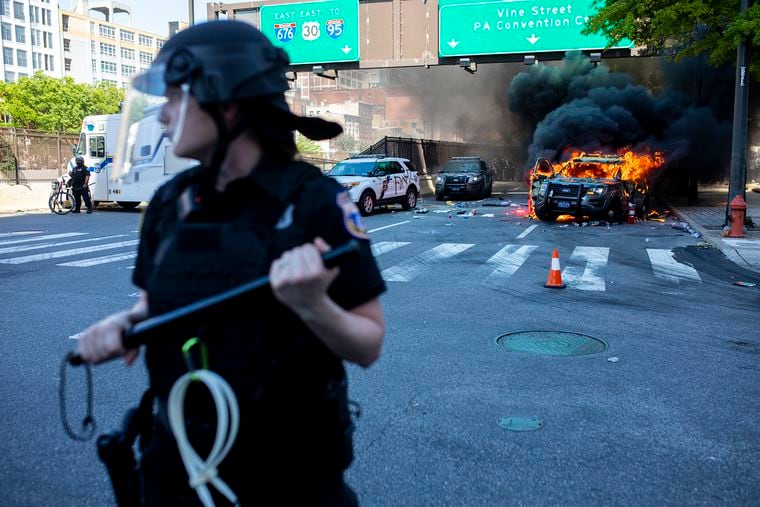 Philadelphia police make a wall to block protestors from approaching a burning Pennsylvania State Police car near the intersection of Broad and Vine Streets during May 30, 2020, protests over the death of George Floyd.