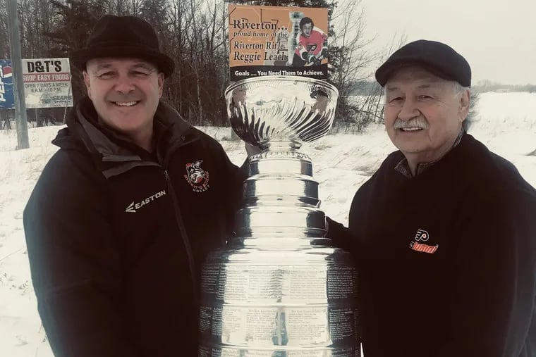 Former NHL player Jamie Leach (left) and his dad, Reggie, a one-time Flyers star, pose with the Stanley Cup in front of a billboard that salutes Reggie.