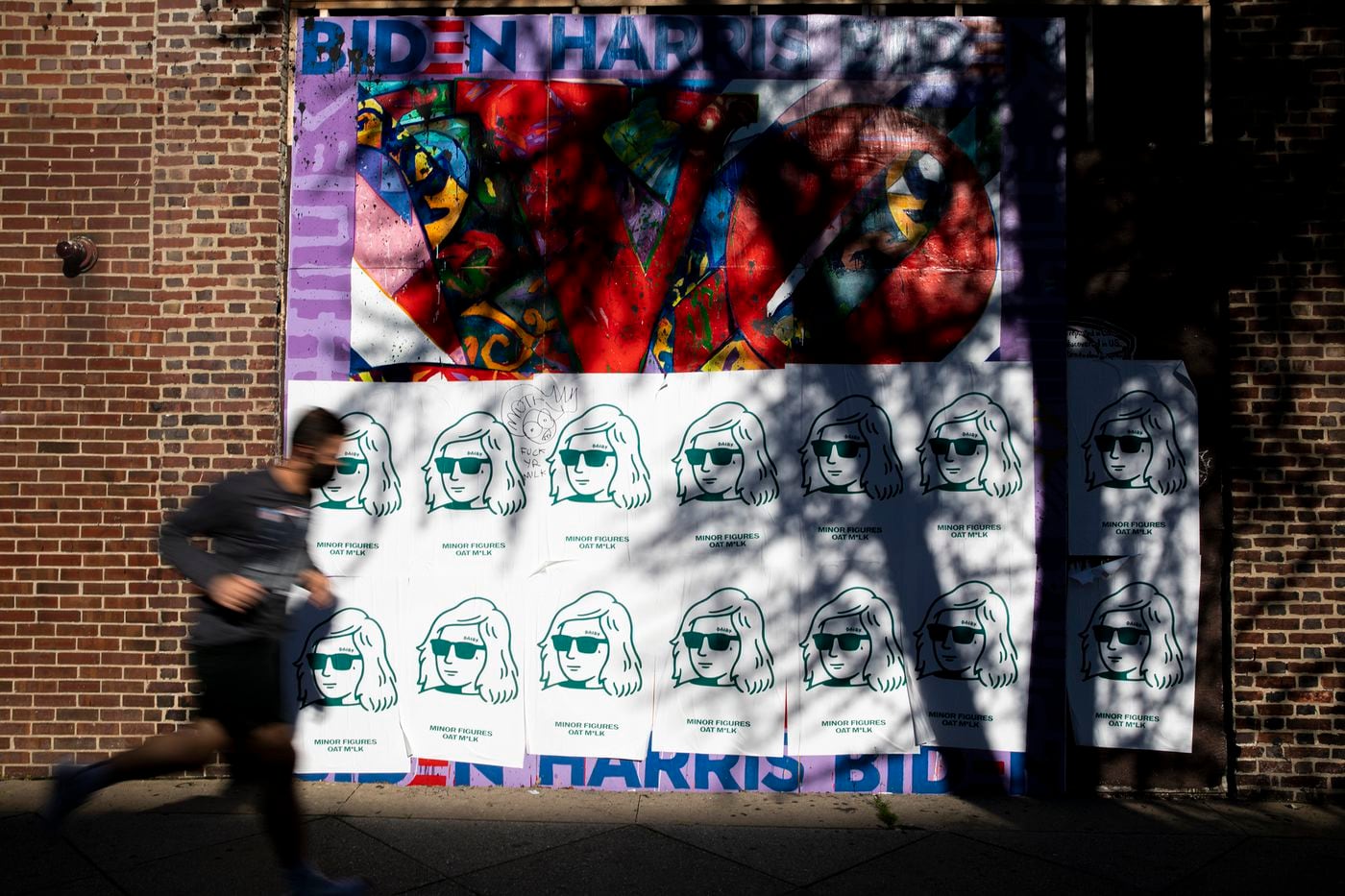 A runner passes by street art covered by plastered advertisement by a London oat milk company along South Broad Street.
