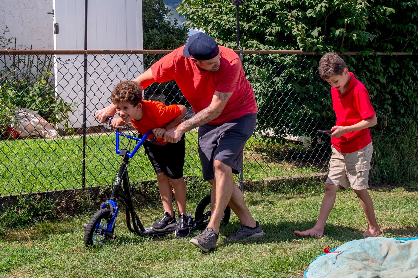 John Barchard helps his partner's son Crosby Akkawi, 8, ride his scooter in the backyard of their Conshohocken home. Behind them is Girius Akkawi, 9. Both boys have Fragile X syndrome.