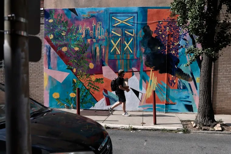 Alex Leon walks past Yuliya Semenova’s mural "Home is Where We Are," on the side of Tuck Barre & Yoga on 7th Street near Rodman in Washington Square West.