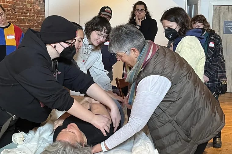 Attendees of a recent shrouding workshop practice on a volunteer, led by Pat Quigley, right, the supervisor of Laurel Hill Funeral Home.