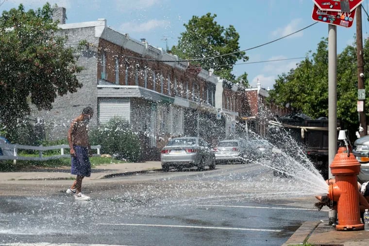 A fire hydrant sprays water in Kensington during a heat wave last July. In Philly's low-income neighborhoods, more than three-quarters of people say they struggle to pay their summer utility bills, but some help exists for certain households without air-conditioning.