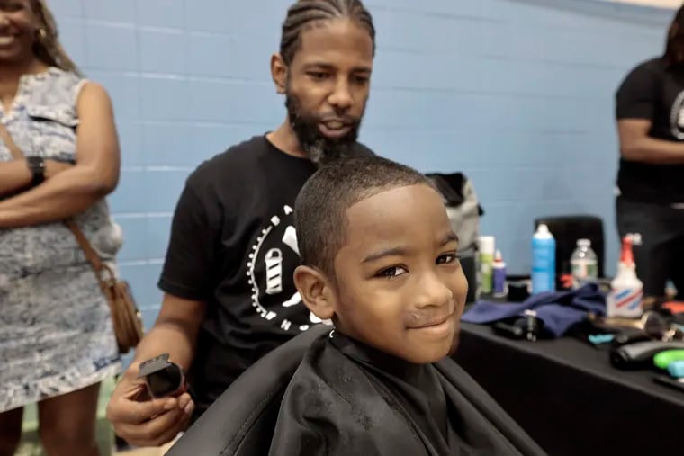 As Chacun McIntyre looks on, her 5-year-old Ethan McIntyre smiles while getting a free haircut from Fadetastic Barber Co. barber Mike Walker at the West Philadelphia YMCA on Sunday.