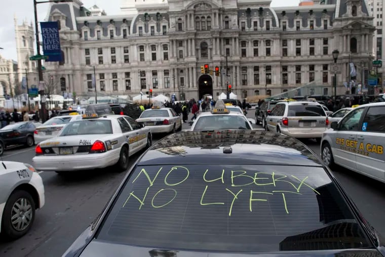 In this February 2016 file photo, taxis and Uber Black cars — one with a message — park in front of City Hall as their drivers demand better regulation of Uber X.