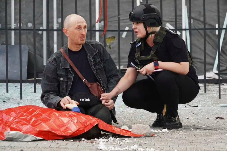 A police officer (right) comforts a man as he holds the hand of his 13-year-old son, who was killed in Russian shelling in Kharkiv, Ukraine, on July 20. The man refused to let emergency workers take his son’s body while he prayed beside it for two hours.