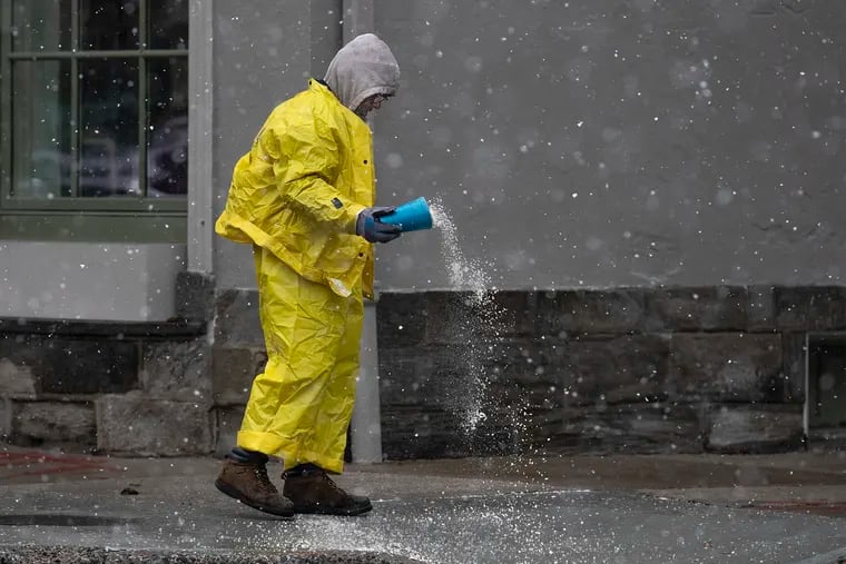 A worker throws salt onto the curb off of Germantown Avenue as a light snow fell in Chestnut Hill early on Dec. 2.