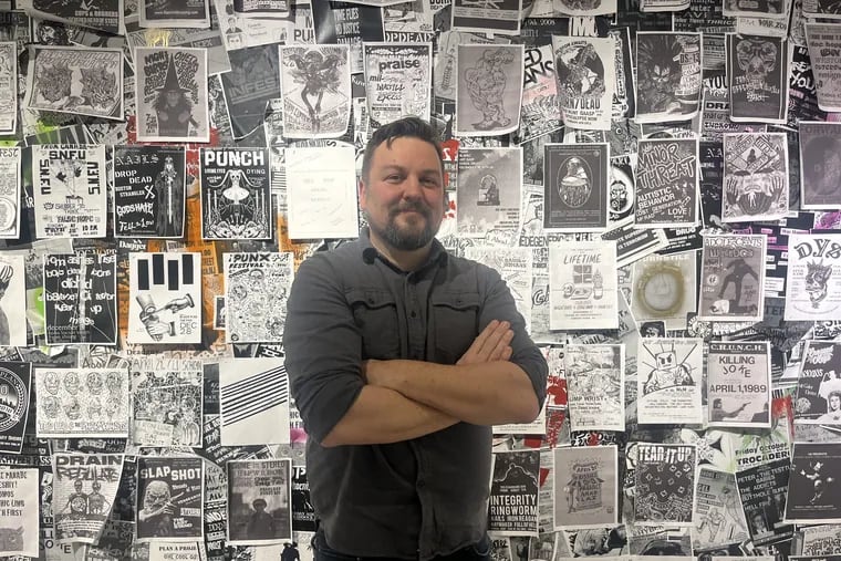 Justin Gray, co-curator of "Shortest, Fastest, Loudest," stands in front of the flier wall at Stockton University.