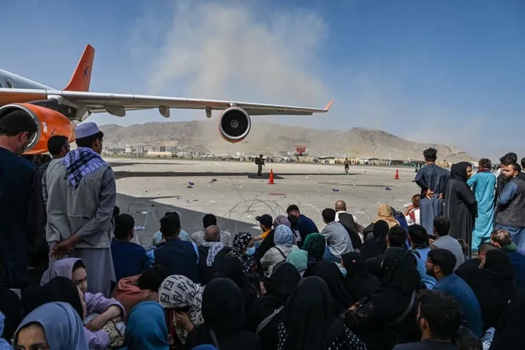 Afghan people sit as they wait to leave the Kabul airport on Aug. 16, 2021, after a swift end to Afghanistan's 20-year war, as thousands of people mobbed the city's airport trying to flee the Taliban's feared hardline brand of Islamist rule.