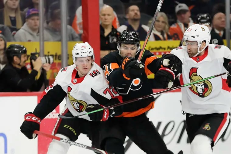 Scott Laughton battles the Ottawa Senators' Thomas Chabot (left) and Colin White (right) on Saturday. The Flyers' forward scored the game-winning goal and contributed an assist and four hits in a 4-3 victory.
