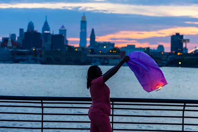 Tiana Cole lights a flying illuminary along the Camden waterfront to mark her late grandmother's birthday, Joyce Cole, on Tuesday, June 25, 2024. Tiana and other family members gathered along the Delaware River but had difficulty with lighting and getting the floating luminaries to fly. 