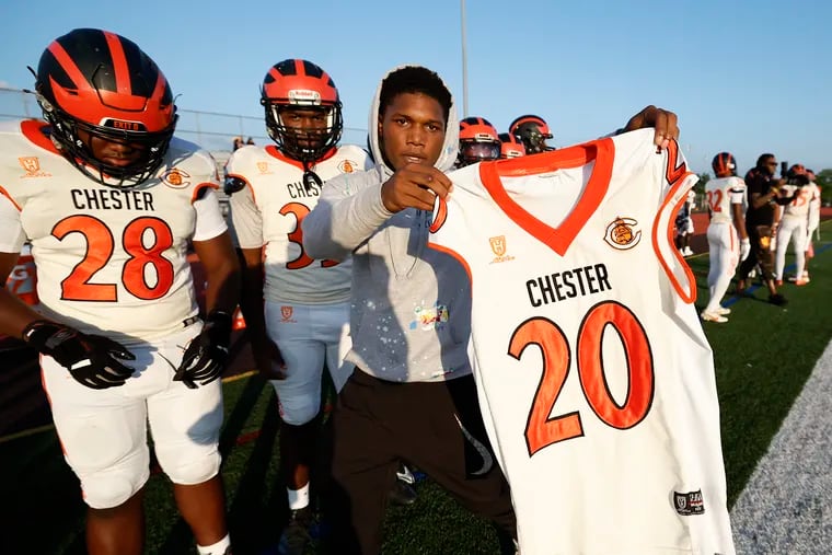 Nahree Melvin (right) holds the jersey of the late Zaheem Sabree while the Chester High School football team opened its season on the road against Perkiomen Valley High School on Aug. 23.