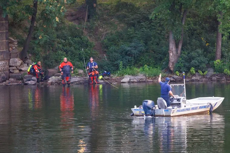 Philadelphia police marine unit officer using hand signal to communicate with others on shore as they look in the Schuylkill River for report of person in car, Friday morning.