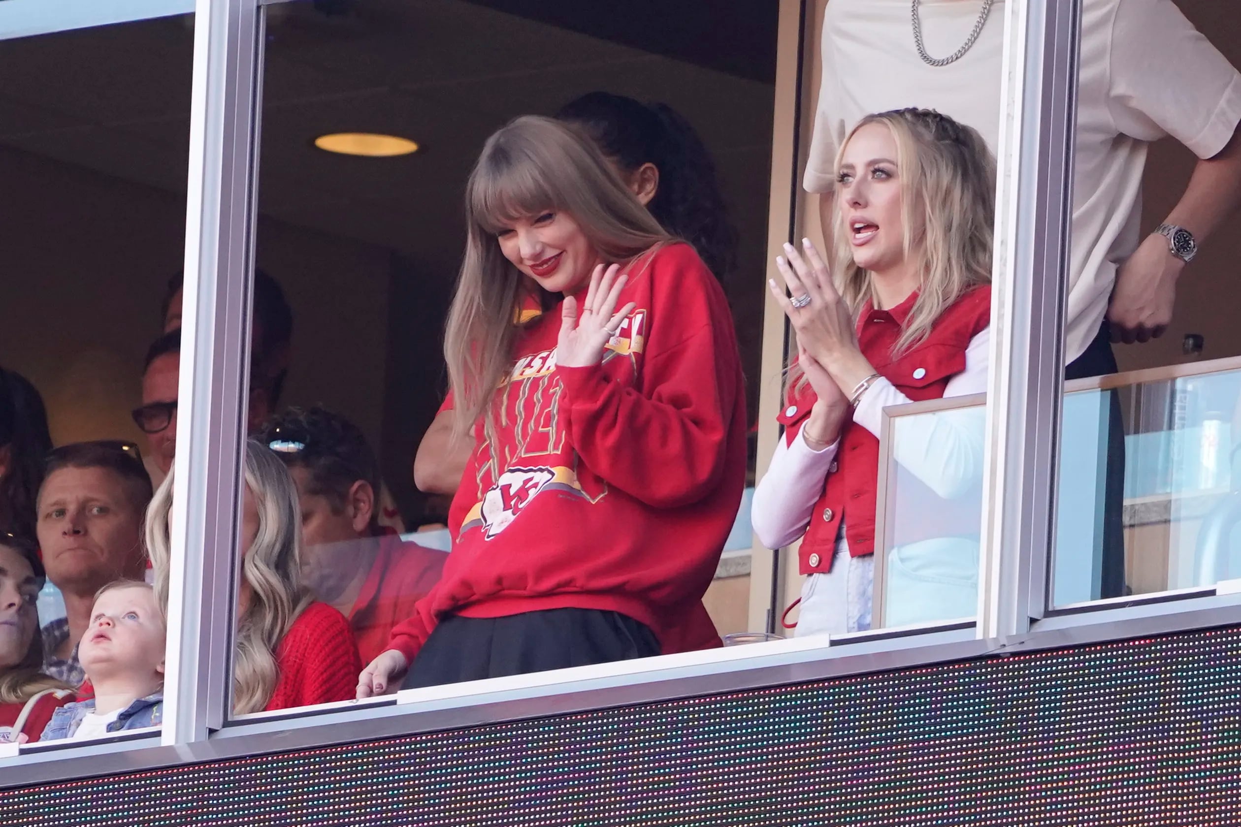 Taylor Swift waves from a suite alongside Brittany Mahomes during a Chiefs game last season. 