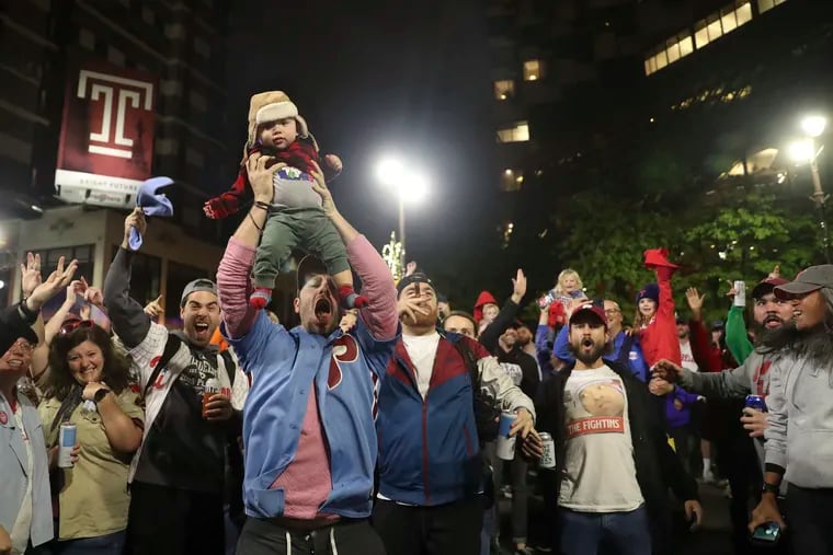 Ben Siegel-Wallace holds up his 9-month old, Elliyas, as fans celebrate at Broad and Locust Streets in Philadelphia after the Phillies defeated the Padres to move on to the World Series on Sunday.