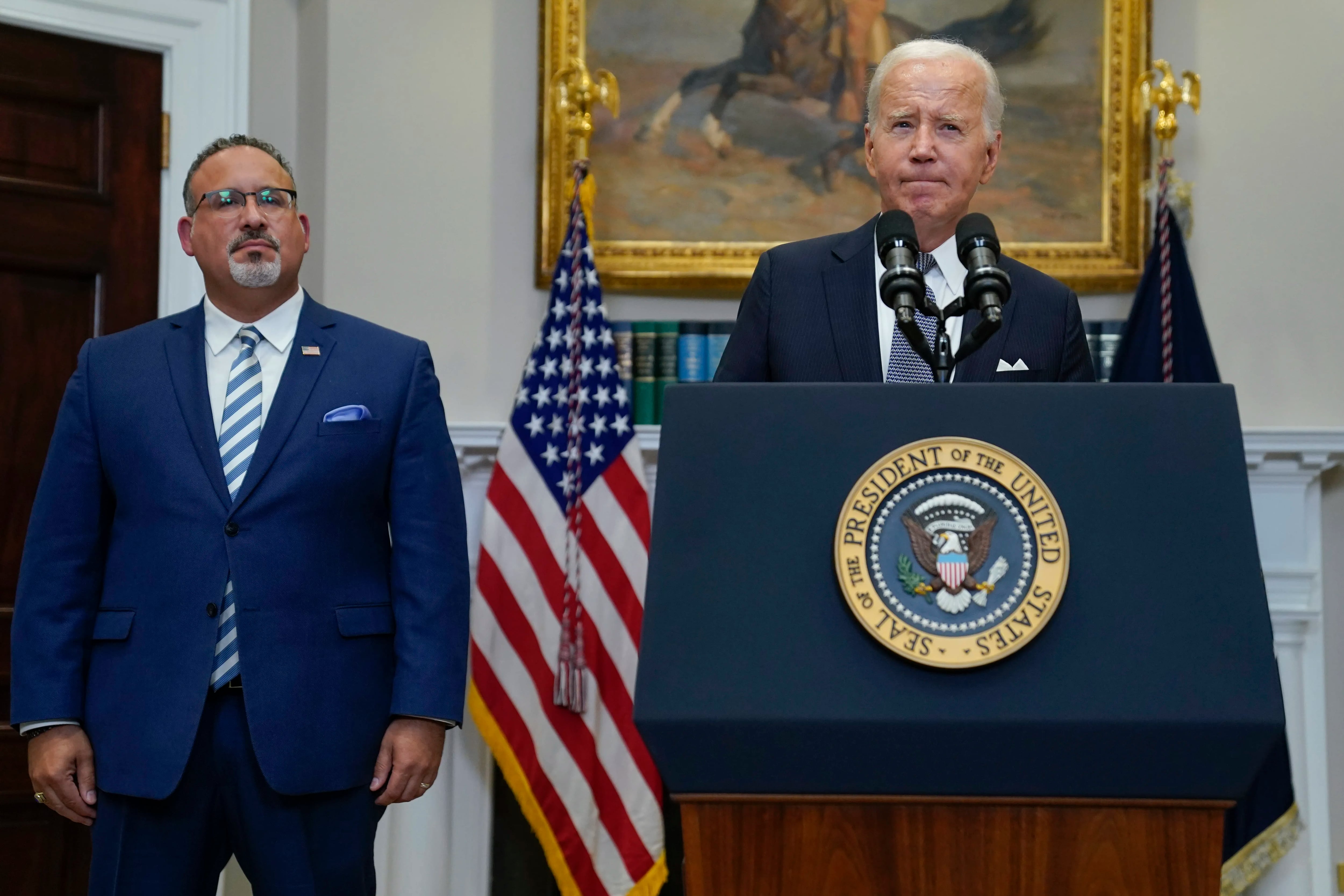 President Joe Biden speaking in the Roosevelt Room of the White House with Education Secretary Miguel Cardona standing next to him in June.