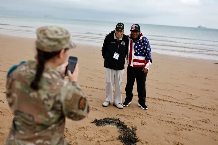 A U.S. soldier takes a photograph of American World War II veteran Sid Edson (center left) during a ceremony on Omaha Beach, Tuesday in Normandy, France. World War II veterans from across the United States, as well as Britain and Canada, are in France to mark 80 years since the D-Day landings that helped lead to Adolf Hitler's defeat.