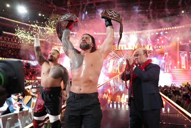 Roman Reigns, center, holds up his WWE heavyweight and universal championship belts after defeating Cody Rhodes in the main event of WrestleMania 39 in April at SoFi Stadium in Inglewood, Calif.