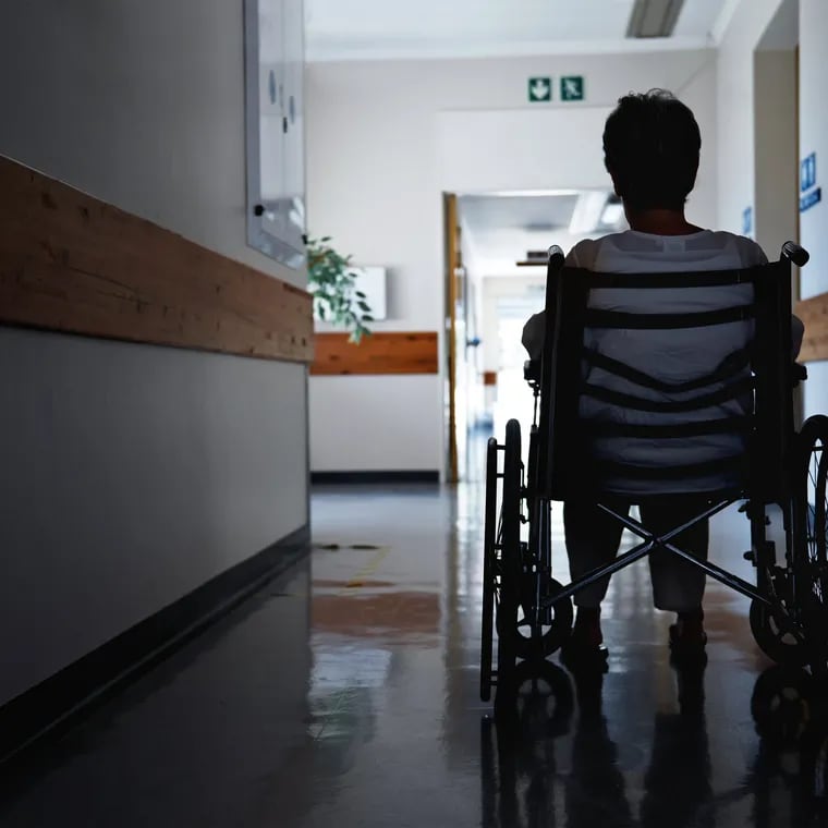 A patient in a wheelchair sits in the hallway of a hospital or nursing home.