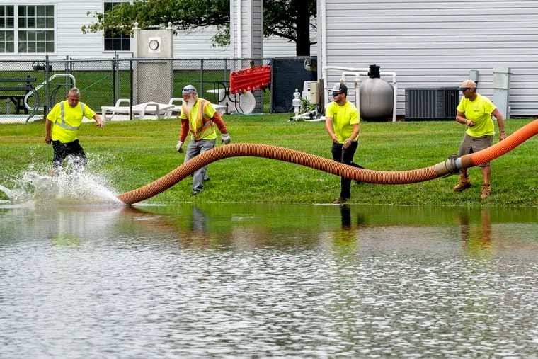 Public works employees drop a pipe into a full water retention pond near the community center in the Silver Park West Estates, a 55-and-older community in Edgewater Park on Wednesday. Some nearby homes were evacuated and cars were abandoned in the Burlington County neighborhood due to flooding.