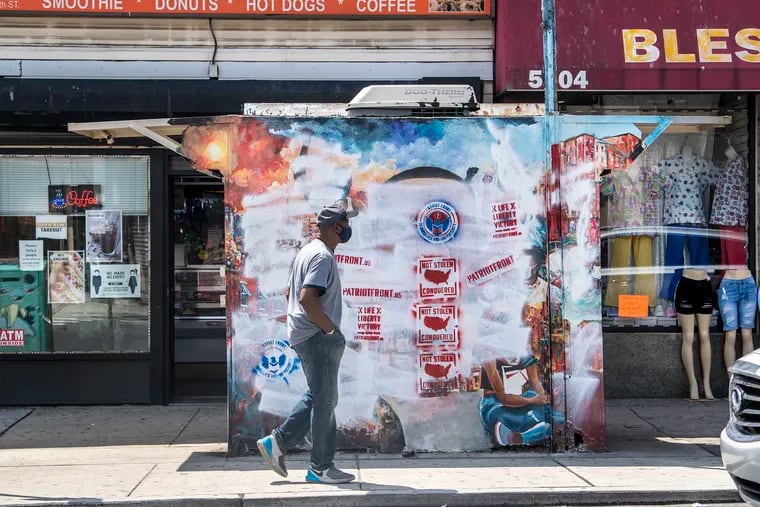 A pedestrian walks in front of a George Floyd mural at 5th and Olney Streets that was vandalized with white nationalist signs.
